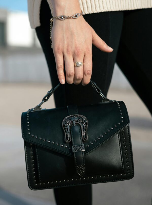 A woman holding a black handbag with studs